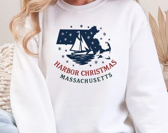 May include: White sweatshirt featuring a navy blue graphic of the Massachusetts state outline with a sailboat and snowflakes. The text "Harbor Christmas Massachusetts" is printed in red and green. The word "WHITE" is printed at the bottom.
