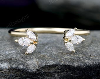 May include: A gold-colored ring with a unique design. The ring features two clusters of white, marquise-cut gemstones, each cluster composed of three stones. The gemstones are set on either side of the ring's band, creating an open design.