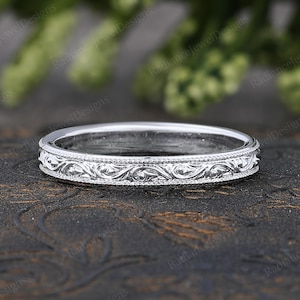 Peut inclure: Une bague en argent avec un motif floral complexe autour du bandeau. La bague a une finition polie et un design délicat. La bague est un bijou, probablement pour un mariage ou des fiançailles.