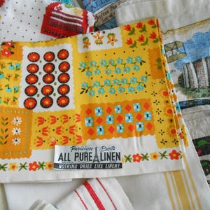 May include: A collection of vintage linen textiles with colorful floral and geometric patterns. The focal point is a yellow linen with orange, red, and blue designs. The text "ALL PURE LINEN" is visible. Other linens feature various patterns.