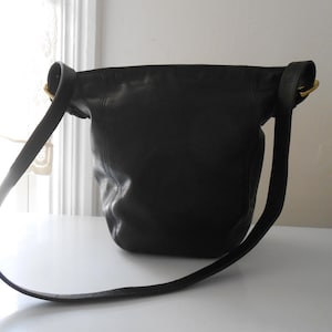 May include: Black leather shoulder bag with a long strap and gold-tone hardware. The bag has a rounded shape and a simple, classic design. The strap is adjustable and appears to be made of the same leather as the bag.