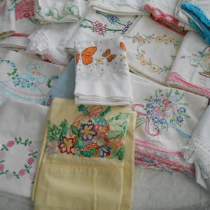 May include: A collection of vintage embroidered linens, including pillowcases and handkerchiefs. The linens feature floral, butterfly, and other decorative embroidery in various colors. Some pieces have lace or crochet trim.