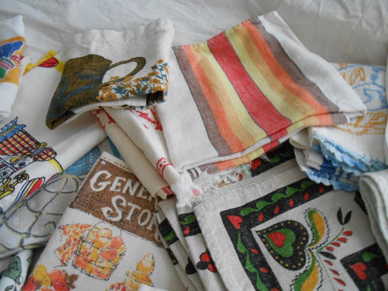May include: A collection of vintage fabric napkins and cloths. Some napkins feature colorful stripes, floral patterns, and text that reads "General Store". Other napkins have images of a teapot, and a blue and white design.