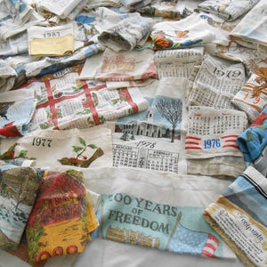 May include: A collection of vintage handkerchiefs with various designs and dates. Some handkerchiefs feature calendar pages from the years 1976, 1977, 1978, 1979, and 1987. Other handkerchiefs have illustrations of birds, landscapes, and patriotic themes.