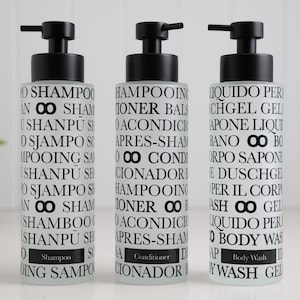 Op de afbeelding: Drie pompflessen van matglas met zwarte pompen. Elke fles heeft zwarte tekst, met de woorden "Shampoo", "Conditioner" en "Body Wash" op de etiketten. Voor gebruik in de badkamer.