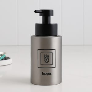 Könnte beinhalten: Ein silberfarbener Handseifenspender mit schwarzer Pumpe. Der Spender hat ein quadratisches Etikett mit den Worten "HAND SOAP" in einem schwarzen Rahmen. Der Markenname "loopa" ist darunter aufgedruckt.