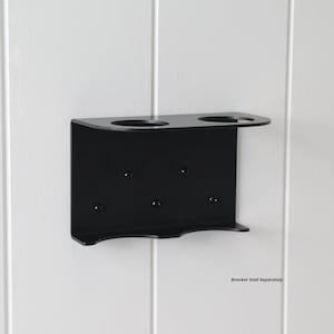 May include: A black metal wall-mounted holder with two circular openings and a small shelf. The holder has several screw holes for mounting. The text "Bracket Sold Separately" is visible at the bottom right.