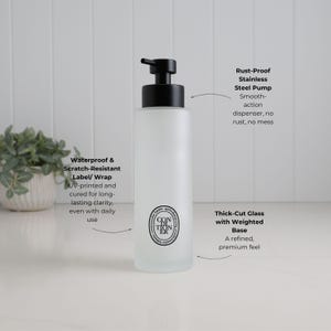 Feature-led image of frosted glass conditioner dispenser highlighting premium build and everyday usability. Showcases smooth rust-resistant pump, durable waterproof UV printed label, and thick weighted base for stability. Refillable bathroom bottle designed for clean dispensing, long-lasting performance, and a refined minimalist look.