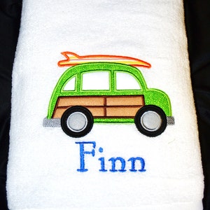 May include: White bath towel with an embroidered green and brown station wagon with an orange surfboard on top. The name "Finn" is embroidered below the car.