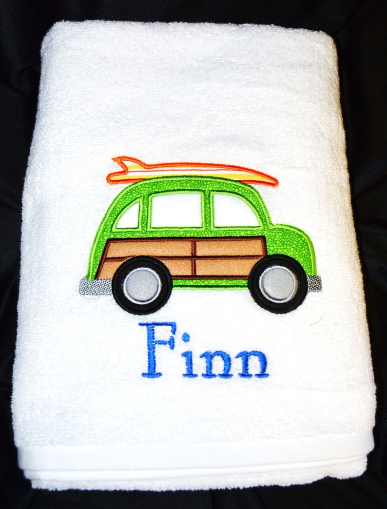 May include: White bath towel with an embroidered green and brown station wagon with an orange surfboard on top. The name "Finn" is embroidered below the car.