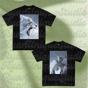May include: Two black t-shirts with animal portraits. One shirt features a roaring lioness in a grayscale painting. The other shirt displays a thoughtful chimpanzee, also in grayscale. The shirts have the text "Ryan Unique Studio".