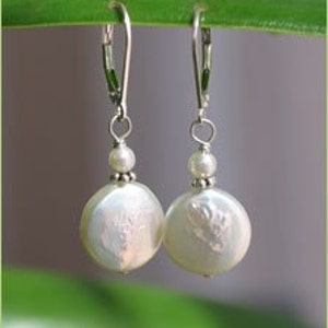 May include: A pair of white pearl dangle earrings with silver hooks. The pearls are round and have a slight iridescent sheen.