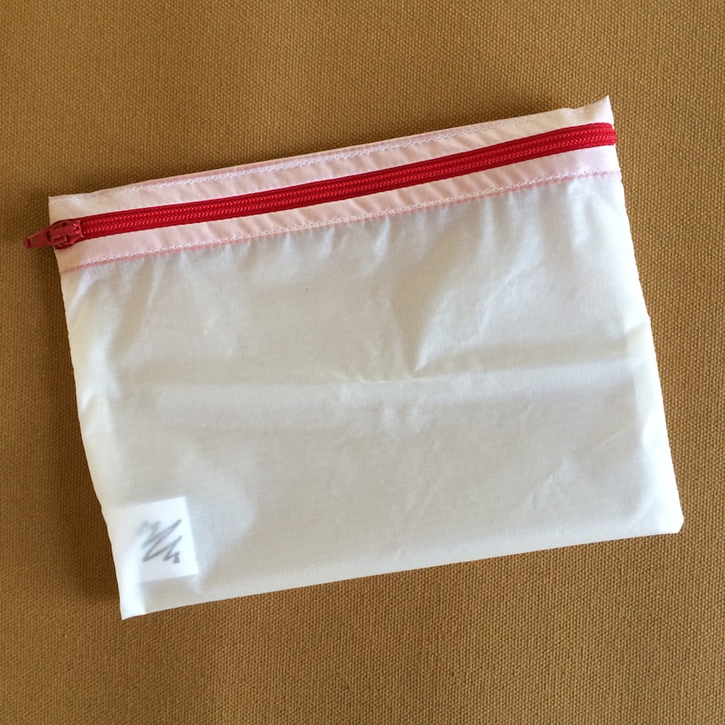 May include: A white mesh zippered pouch with a pink and red zipper. The pouch has a small white label with a scribble on it.
