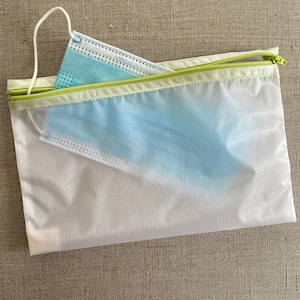 May include: A white mesh zippered pouch with a light blue face mask inside. The pouch has a green zipper.