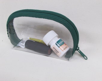 May include: A clear plastic zippered pouch with a green trim. The pouch contains a small bottle of Bayer Aspirin, a black tube, and a small white tube.