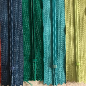 May include: Five zipper tapes in different colors: dark blue, green, teal, light blue, and light green. The zipper tapes are all the same size and have a smooth texture.