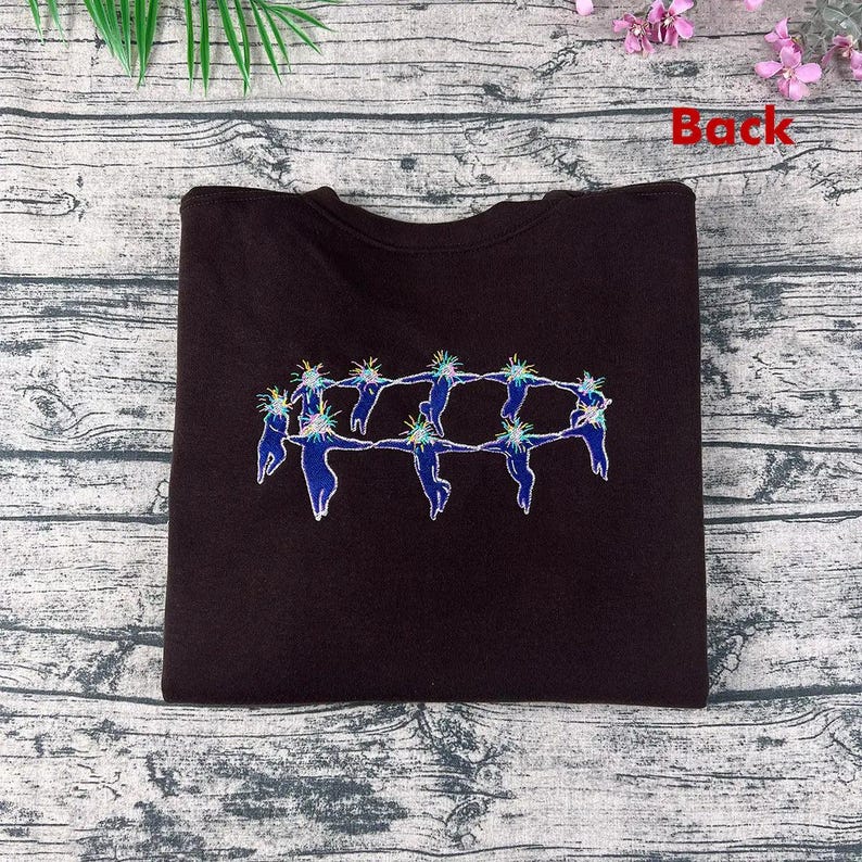 May include: A dark brown sweatshirt featuring an embroidered design of figures holding hands in a circle. The figures are blue with white outlines and have colorful, spiky hair. The word "Back" is printed in red.