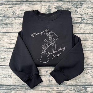 Op de afbeelding: Zwart sweatshirt met witte lijntekening van een stel en de tekst "There you are, I've been looking for you". Het ontwerp toont een man en een vrouw in historische kleding, waarbij de man een licht vasthoudt.