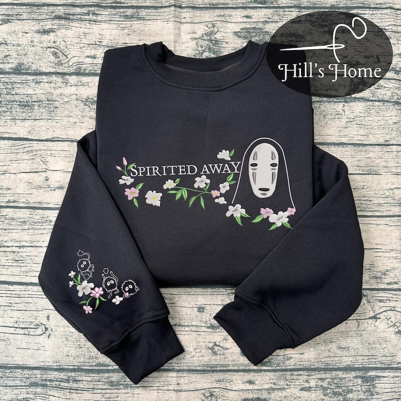 Puede incluir: Sudadera negra con un dise&ntilde;o bordado de la pel&iacute;cula "El Viaje de Chihiro". El dise&ntilde;o incluye el texto "Spirited Away", un personaje y detalles florales en blanco, rosa y verde. La manga tambi&eacute;n tiene un peque&ntilde;o dise&ntilde;o bordado.