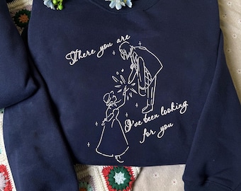 May include: A navy blue crewneck sweatshirt featuring a white line art illustration of two figures reaching toward each other with sparkling accents. The text reads, There you are, I've been looking for you, written in a cursive script font.