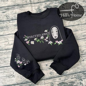 Puede incluir: Sudadera negra con detalles florales bordados y el texto "Spirited Away". El dise&ntilde;o incluye un personaje de la pel&iacute;cula de animaci&oacute;n. La manga tiene personajes y flores bordadas adicionales.