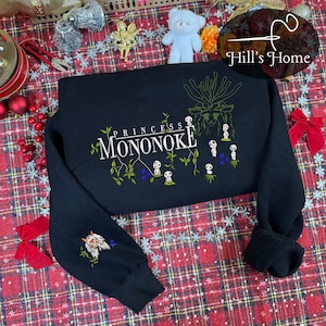 Pu&ograve; includere: Felpa nera con la scritta "Princess Mononoke" e un'illustrazione dello spirito della foresta e dei Kodama. La manica sinistra presenta un'immagine ricamata di una creatura simile a un lupo. Il design include accenti verdi, bianchi e blu.