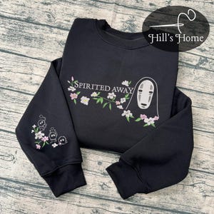 Puede incluir: Sudadera negra de cuello redondo con dise&ntilde;o bordado. Presenta el texto "Spirited Away" con una rama floral y un personaje de la pel&iacute;cula. La manga izquierda tiene un dise&ntilde;o bordado de tres peque&ntilde;os personajes y flores.