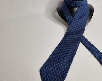 以下が含まれることがあります： 白の小さな模様が入った青い模様のネクタイ。ネクタイは黒いネクタイスタンドに結ばれています。