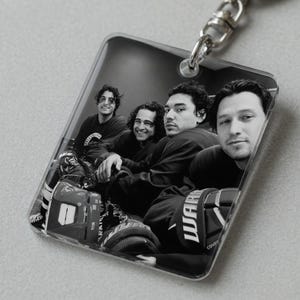 May include: A clear, rectangular keychain featuring a black and white photograph of four people. The image includes hockey equipment and the word "WAR" on a glove. A silver-colored keyring is attached to the top.