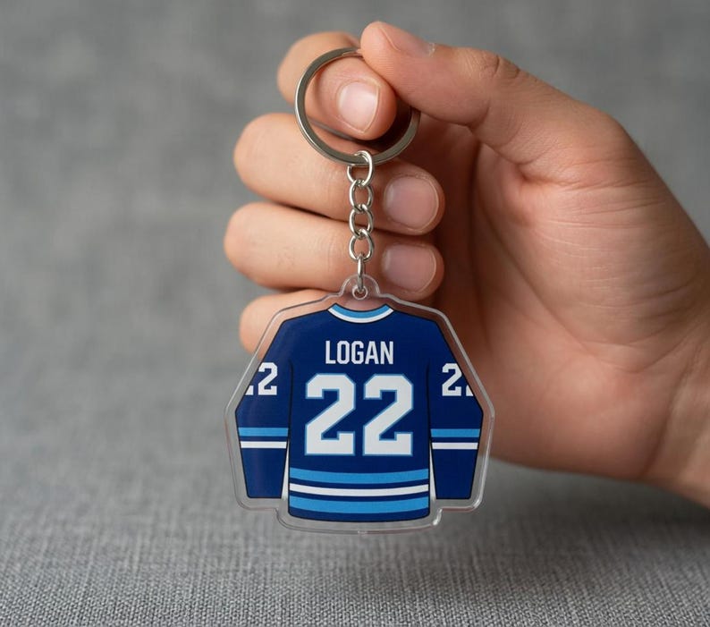 May include: A clear acrylic hockey jersey-shaped keyring. The navy blue jersey features white and light blue stripes and the number 22. The name "LOGAN" is printed above the number.