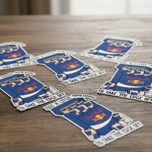 May include: Several stickers featuring a blue and white cartoon design of a Red Bull carton with cans. The stickers have the text "TO TAKE THE EDGE OFF" and "JUST A LITTLE SOMETHING".