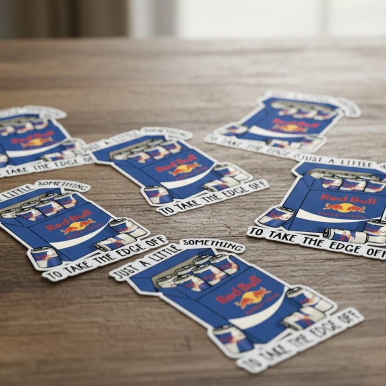 May include: Several stickers featuring a blue and white cartoon design of a Red Bull carton with cans. The stickers have the text "TO TAKE THE EDGE OFF" and "JUST A LITTLE SOMETHING".