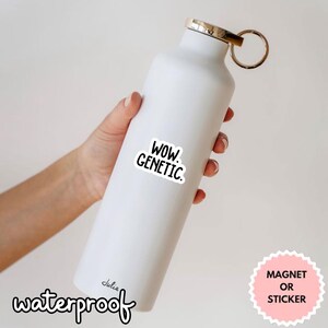 Op de afbeelding: Een witte ge&iuml;soleerde waterfles met een goudkleurige dop en een zwart-witte sticker met de tekst "WOW. GENETIC." Het woord "waterproof" is in cursief geschreven. Een roze sticker zegt "MAGNEET OF STICKER."