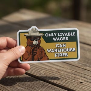 May include: A rectangular sticker featuring Smokey Bear with the text "ONLY LIVABLE WAGES CAN WAREHOUSE FIRES." The sticker has a white border, a yellow background, and a green banner. Smokey Bear is wearing a ranger hat.