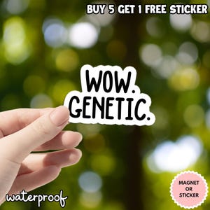 Op de afbeelding: Een witte sticker met de woorden "WOW. GENETIC." in het zwart, tegen een vage groene achtergrond. De sticker is waterdicht en de tekst "BUY 5 GET 1 FREE STICKER" staat bovenaan. Een roze sticker zegt "MAGNET OR STICKER."