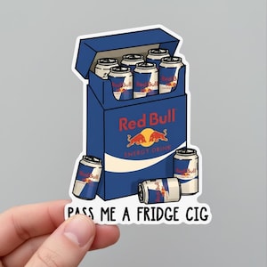 May include: A sticker featuring a cartoon illustration of a blue Red Bull box with six cans inside and two outside. The text "Red Bull ENERGY DRINK" and "PASS ME A FRIDGE CIG" are also visible.