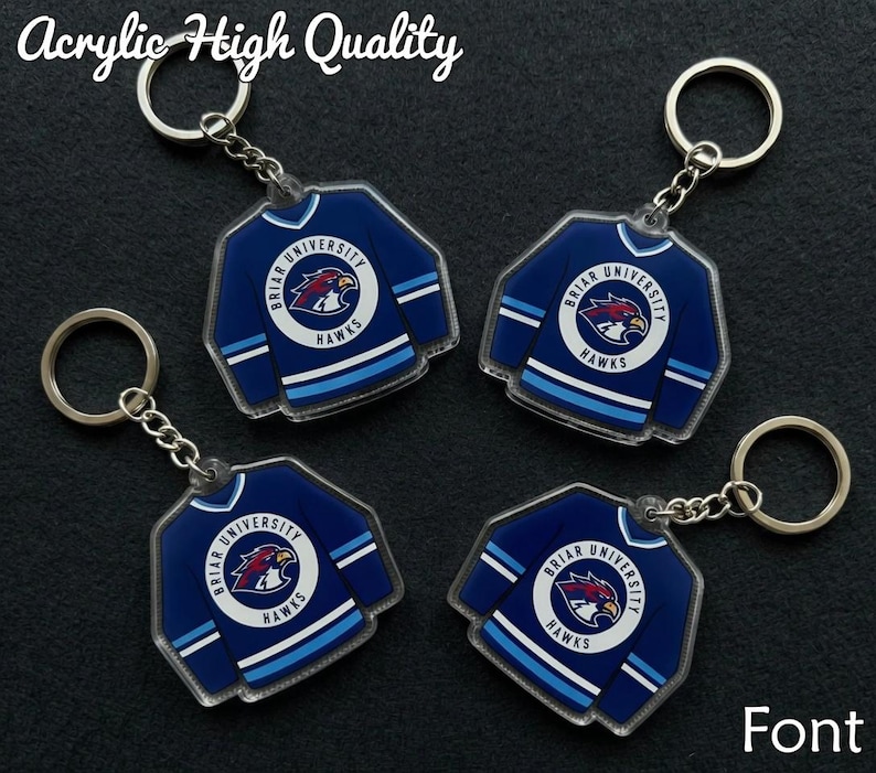 May include: Four acrylic keyrings shaped like blue hockey jerseys with white and light blue stripes. Each keyring features the text "Briar University Hawks" and a hawk logo. The text "Acrylic High Quality" is at the top.