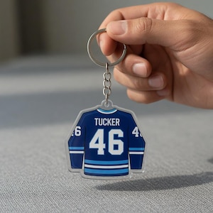 May include: A blue and white hockey jersey keyring with the name "Tucker" and the number "46" printed on it. The keyring is attached to a silver chain.