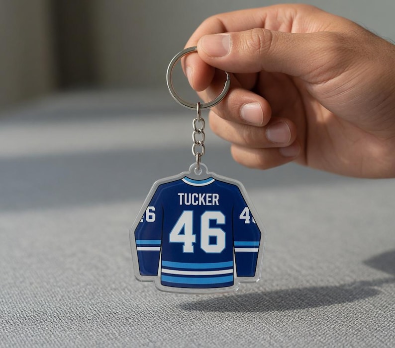 May include: A blue and white hockey jersey keyring with the name "Tucker" and the number "46" printed on it. The keyring is attached to a silver chain.