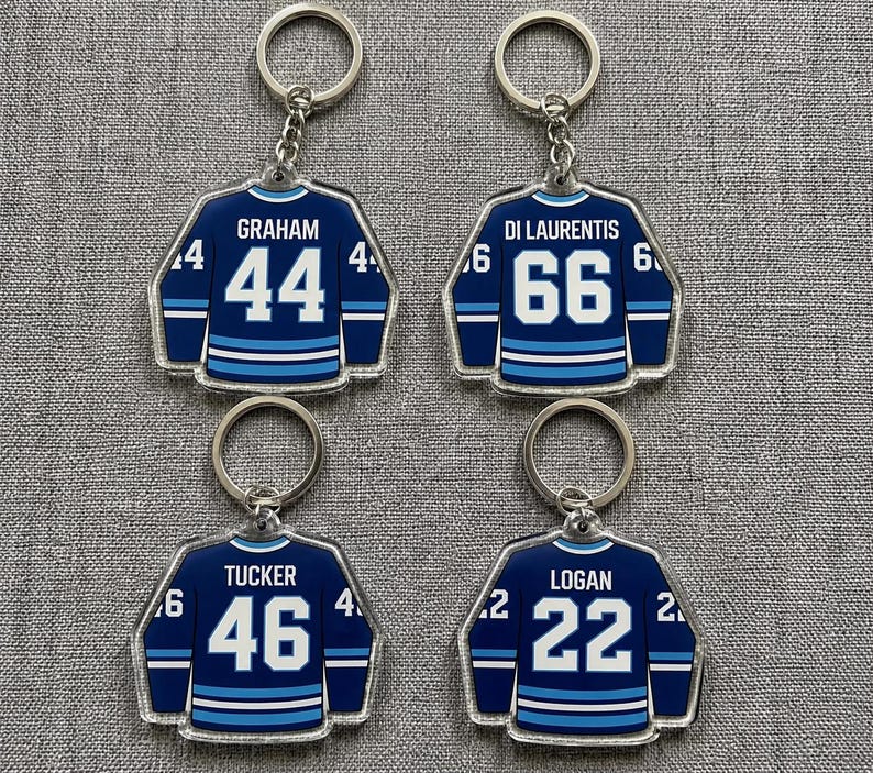 May include: Four hockey jersey keyrings. Each keyring is navy blue with white and light blue stripes, displaying a player's name and number. The names are Graham, Di Laurentis, Tucker, and Logan. The numbers are 44, 66, 46, and 22.