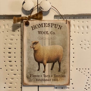May include: A rustic wooden sign with the text "Homespun Wool Co." and a picture of a sheep. The sign also says "Fleece * Yarn * Textiles Established 1805".