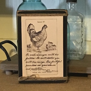 May include: A framed print with a black border and a light brown background. The print features a black and white illustration of a hen and chicks with the text "He will cover you with his feathers. He will shelter you with his wings, the faithful promises are your armor and protection. Look how they run when she calls them!"