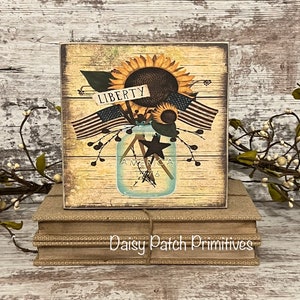 May include: A wooden sign with a rustic background featuring a mason jar filled with sunflowers and American flags. The jar has the words "America 1776" on it. The sign also has a small sign that says "Liberty".