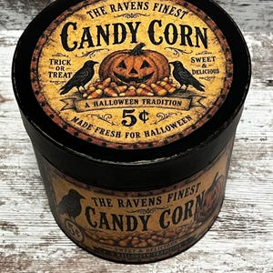May include: A round black container with a vintage-style label featuring a jack-o'-lantern, two black ravens, and candy corn. The text reads: THE RAVENS FINEST CANDY CORN, TRICK OR TREAT, SWEET & DELICIOUS, A HALLOWEEN TRADITION, 5&cent;, MADE FRESH FOR HALLOWEEN.