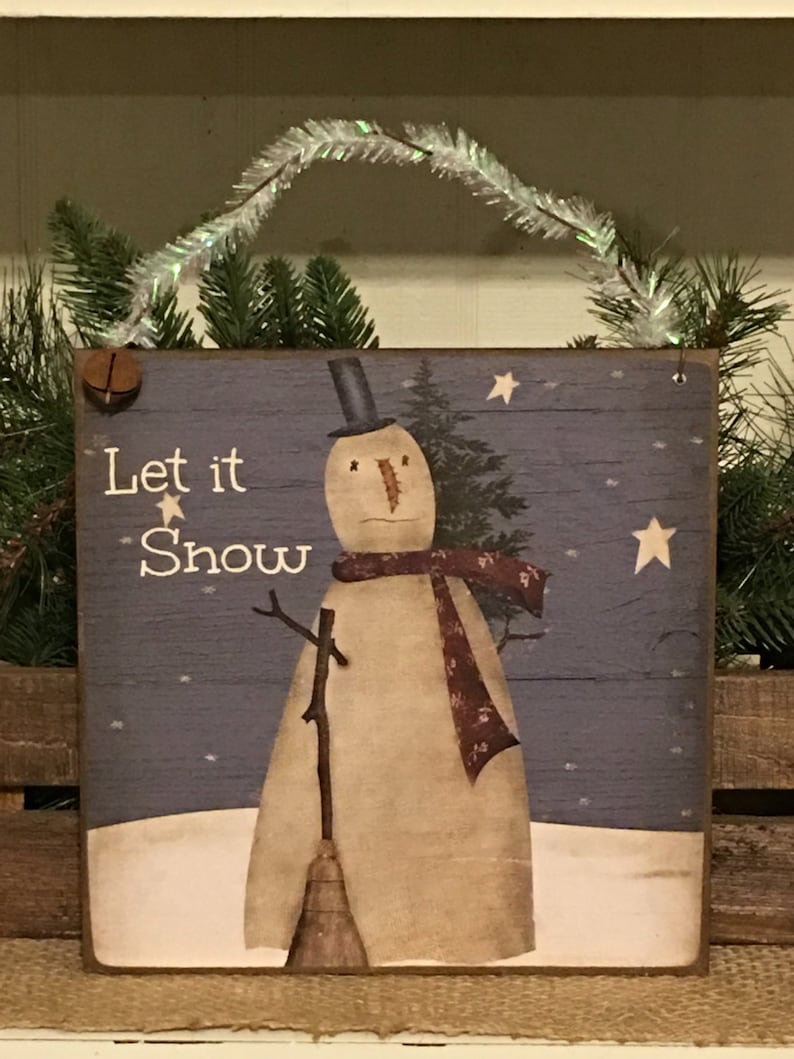 May include: Wooden sign with a snowman illustration and the text "Let it Snow". The snowman wears a black top hat and a patterned scarf. The background is a blue night sky with stars and a snow-covered ground.