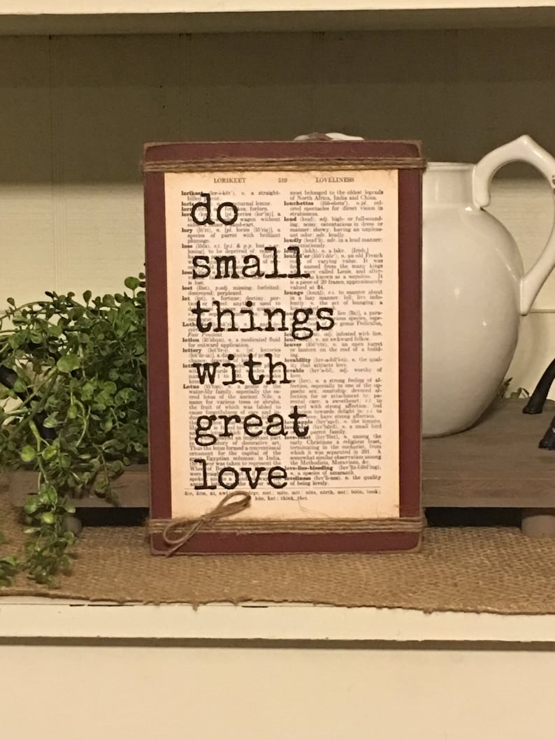 May include: A rustic wooden sign with a red background and a dictionary page overlay. The sign features the quote "Do small things with great love."