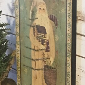 May include: A rectangular wooden sign with a vintage illustration of Father Christmas. The artwork shows Father Christmas in a long cream coat, holding a small tree and a basket. The background is a faded green with snowflake accents, and the border has a decorative pattern.