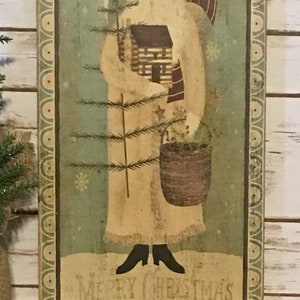 May include: A distressed wooden Christmas sign with a folk art image of Santa Claus. Santa is in a cream robe, holding a house and basket. The sign has a green background with snowflakes and the words "Merry Christmas" at the bottom.