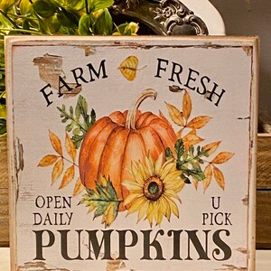 May include: A rustic wooden sign with a distressed white background features a watercolor illustration of a pumpkin and sunflower. The sign reads "Farm Fresh Pumpkins" with "Open Daily U Pick" text.