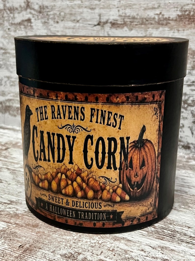 May include: A round black container with a vintage-style label featuring a black raven, a pile of candy corn, and a jack-o'-lantern. The text reads: The Ravens Finest Candy Corn, Sweet & Delicious, A Halloween Tradition.